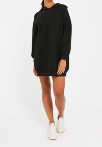 Svart oversized hoodieklänning med framficka och präglad "GUESS"-logotyp. Har långa ärmar och dragsko i huvan. Passar bra med vita sneakers.