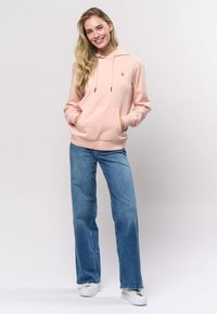 Roza jopa iz bombažne mešanice z žepom spredaj, kapuco z vrvico in majhnim logotipom. Kombinirana s svetlo modrimi širokimi kavbojkami in belimi supergami.