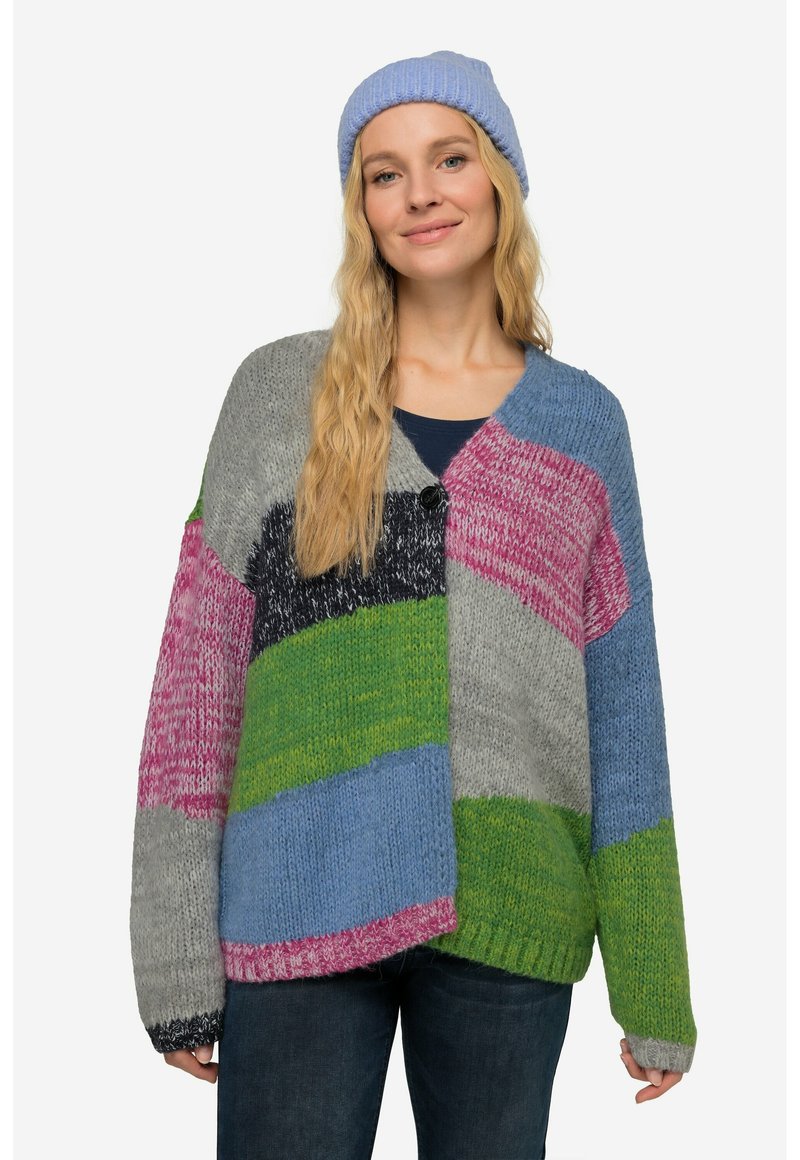 Yksivärinen ylisuuri neulepusero, jossa on harmaita, sinisiä, vihreitä, vaaleanpunaisia ja mustia paloja, V-pääntiellä ja nappidetaljilla. Yhdistetty vaaleansiniseen myssyyn.