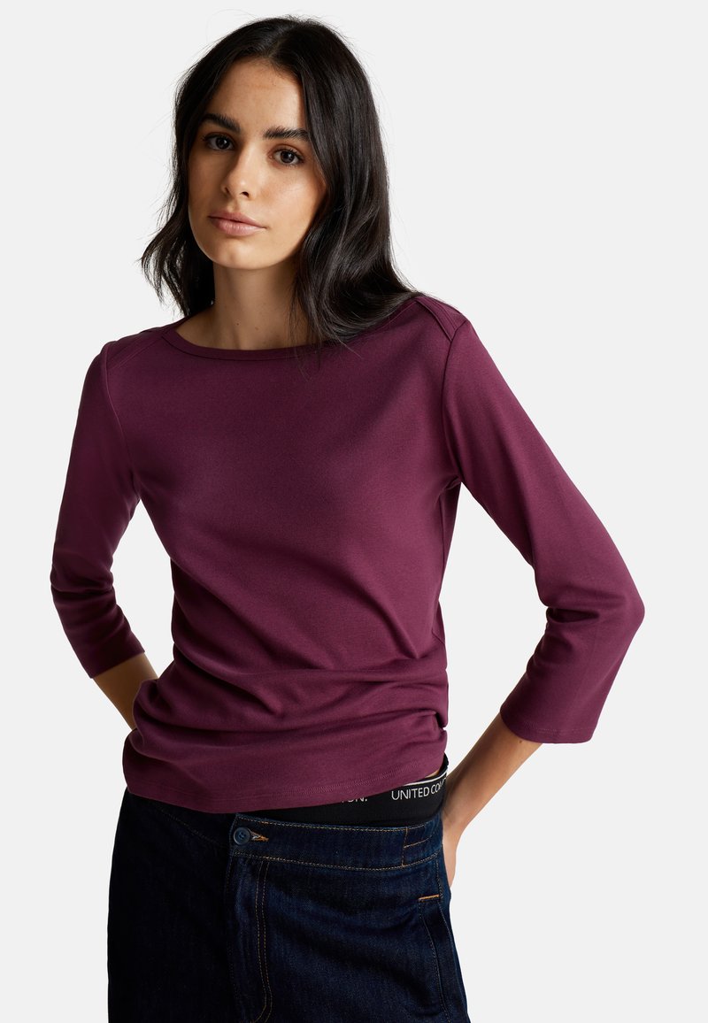 T-shirt bordeaux à manches trois-quarts en tissu doux avec un col rond et une texture lisse, associé à un jean foncé avec une taille visible.