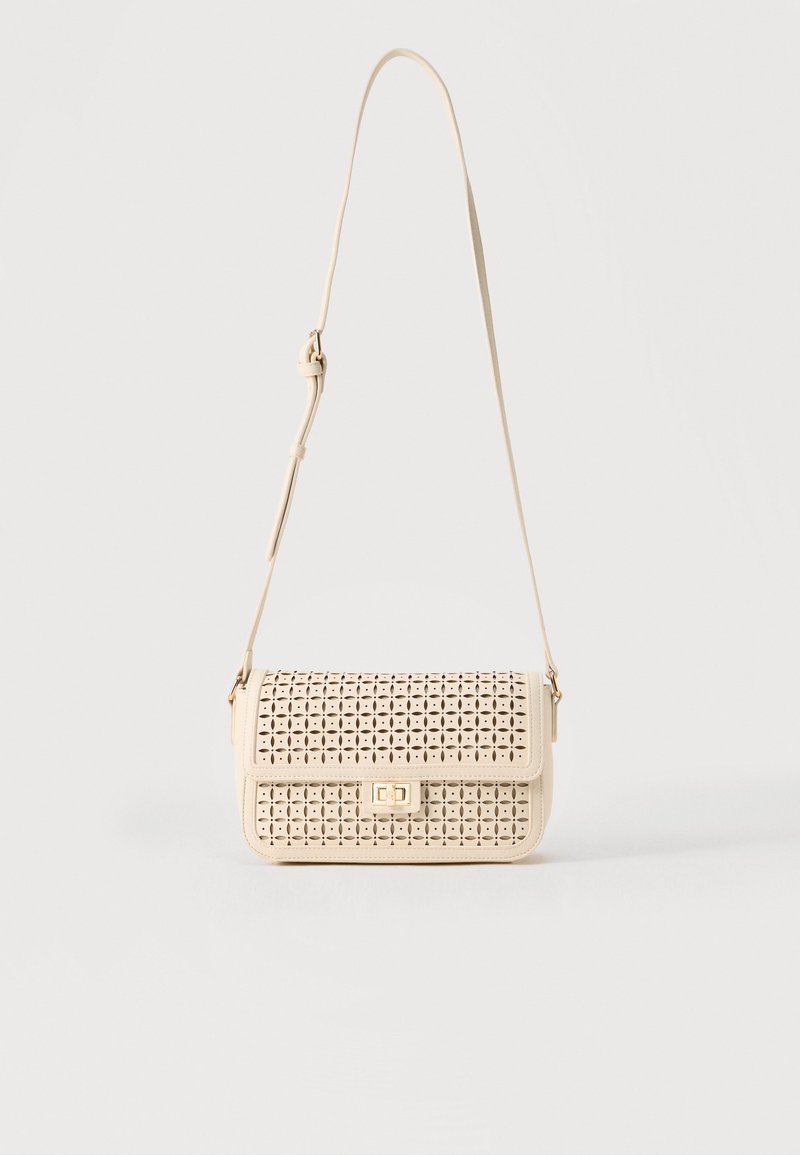 Μπεζ τσάντα ώμου με διάτρητο λουλουδένιο σχέδιο, κλείσιμο με καπάκι, ορθογώνιο σχήμα και ρυθμιζόμενο λουράκι.