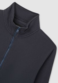 Giacca zip-up grigio scuro con colletto alto. Realizzata in tessuto morbido, presenta una cerniera blu a contrasto e cuciture piatte per una finitura liscia.