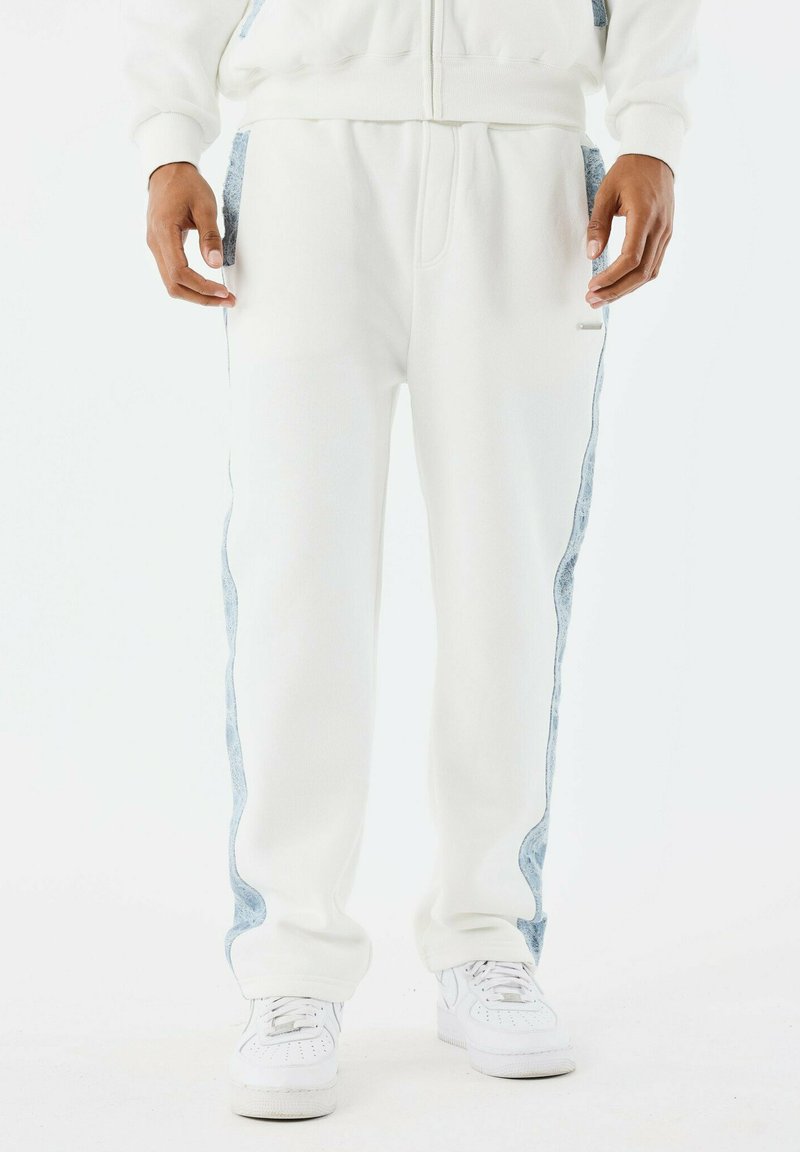 Witte joggers van een katoenmix, met lichtblauwe denim zijpanelen, elastische taille en ribgebreide boorden. Gecombineerd met witte sneakers.