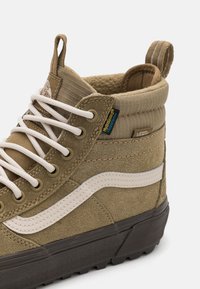 Baskets hautes en daim et tissu beige avec lacets blancs, bande latérale blanche, semelle noire et col rembourré étiqueté HydroGuard imperméable.