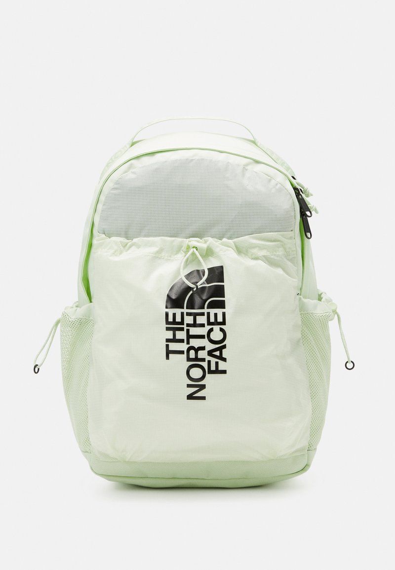 Sac à dos The North Face vert clair avec poche zippée à l'avant, poches latérales en mesh, poignée supérieure et logo noir sur la poche avant.
