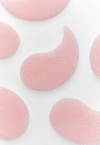 Patchs oculaires en gel de couleur rose pâle, présentant une surface texturée et une forme incurvée de haricot. Différentes tailles sont dispersées sur un fond blanc.