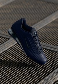 Mornarska tenisica s teksturiranim gornjim dijelom, s crnim swoosh logom, vezanjem sprijeda, podstavljenim okovratnikom i prozirnom sole.