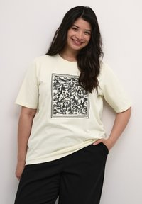 Light yellow short-sleeve t-shirt featuring a black abstract print in a square frame. Relaxed fit with a round neckline.