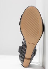 Černobílá tkaná podrážka sandálové obuvi s hnědou gumovou základnou a drážkami pro lepší grip, na které je vyražené logo značky "ALDO."