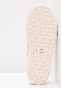 Semelle de sneaker Puma rose clair avec un motif de semelle géométrique et le logo Puma sur une surface blanche contre un fond blanc.