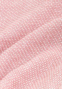 Tela rosa texturizada con un patrón tejido y acentos blancos. El material muestra una apariencia suave y estratificada.
