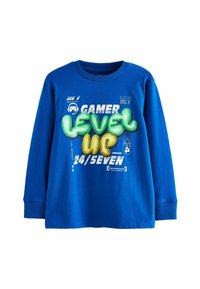Kék, hosszúujjú pamut póló. Élénk zöld és sárga grafikai felirattal rendelkezik: "GAMER LEVEL UP 24/SEVEN." Bordás nyakkivágás és mandzsetta.