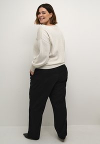 Pull en maille gris clair avec des détails côtelés sur les épaules, associé à un pantalon large noir, sur fond uni clair.