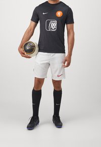 Svart Nike fotbollströja med prickmönster och lejon grafik, tillsammans med vita shorts, svarta strumpor och en fotboll i handen.