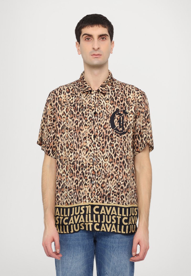 Camisa de manga corta con estampado de leopardo en tonos marrón y negro, que presenta un logo negro en el pecho y una banda negra con patrón en el dobladillo.