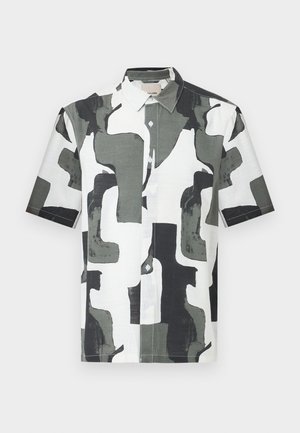 Koszula na guziki z krótkim rękawem w abstrakcyjny, geometryczny wzór w kolorach czarnym, białym i szarym, z ostro zakończonym kołnierzem na jasnym tle.