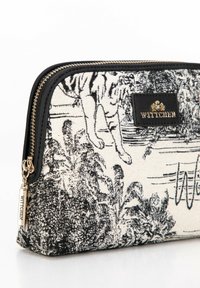 Bolsa de tela en blanco y negro con un patrón de tigre y follaje, con un ribete de cuero negro y herrajes dorados. Cierre de cremallera con una etiqueta de logo.