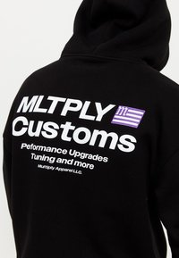 Schwarzer Hoodie mit großen weißen Text "MLTPLY Customs" und lila Akzenten. Besitzt eine weiche Textur und eine Kapuze für Wärme.