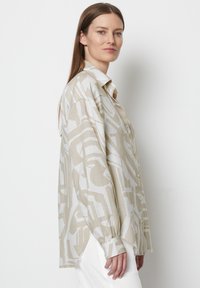 Light beige shirt with abstract white patterns, collared design, button-up front, long sleeves with fitted cuffs, and a loose fit.
