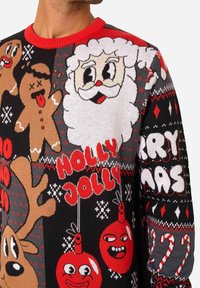 Pleteni božićni džemper s motivima Djeda Božićnjaka, sobova i kolačića u crvenoj, crnoj i sivoj boji, s igrivim tekstualnim elementima i detaljima.