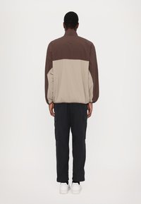 Lehká bunda v hnědé a béžové barvě s vysokým límcem, elastickým lemem a dlouhými rukávy. Kombinováno s černými cargo kalhotami a bílými teniskami.