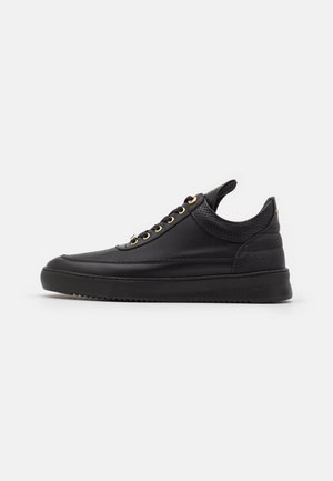 Zapatilla negra con parte superior de malla, ojales dorados y suela texturizada. El diseño incluye una lengüeta en el talón para facilitar el uso.