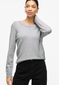 Pilkas megztinis su apvalia iškirpte, ribotais rankogaliais ir laisvo silueto, derinamas su juodomis kelnėmis. Minkšta tekstūra ir paprastas dizainas.