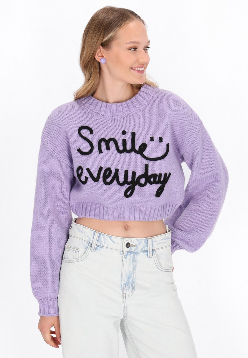 Haken trui in lavendel met zwarte tekst "Smile everyday", geribbelde zoom en lange mouwen. Gemaakt in combinatie met licht gewassen, high-waisted spijkerbroek.