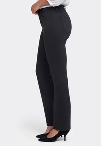 Mörkgrå byxor med smal passform, slät textur, sidofickor och raka ben, kombinerade med svarta högklackade skor.