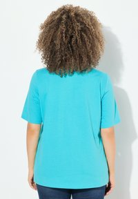 T-shirt turchese a maniche corte con scollo rotondo e una texture liscia, visto da dietro, abbinato a jeans scuri.