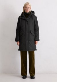 Czarna ocieplana kurtka z kapturem, z zamkiem błyskawicznym z przodu, zatrzaskami, dwiema bocznymi kieszeniami i regulowanymi sznurkami. W komplecie z oliwkowymi spodniami z kordurowej tkaniny.