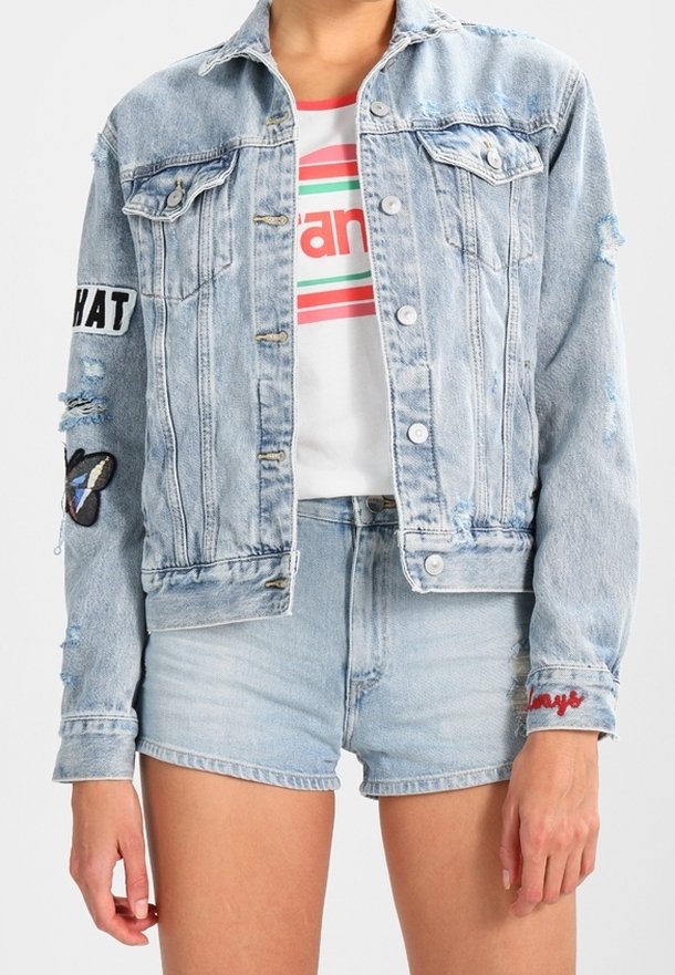 Giacca in denim azzurro chiaro con finitura sbiadita, chiusura a bottoni, tasche frontali e toppe ricamate a forma di farfalla e con testo sulle maniche.