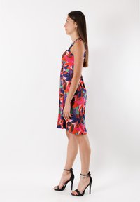 Kädetön mekko kirkkaan kukkakuosin kanssa, jossa on punaisia, vihreitä ja tummansinisiä värejä; pehmeää kangasta, A-linjainen malli ja polvipituinen, pukeutuneena mustiin korkeisiin korkoihin.