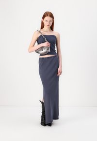 Completo a due pezzi composto da un top blu navy senza maniche e una gonna lunga coordinata. La modella porta una borsa a spalla in metallo argento. Stivali neri fino al ginocchio.