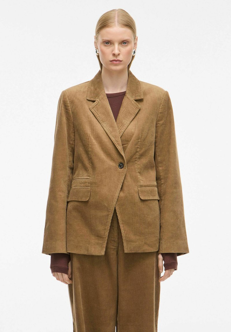 Blazer en velours côtelé marron avec deux poches avant, revers crantés et fermeture à un bouton ; coupe près du corps avec une surface texturée.