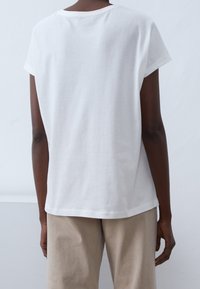 Vit bomulls t-shirt med korta ärmar, avslappnad passform, rund halsringning och slät yta, visas bakifrån mot en ljus bakgrund.