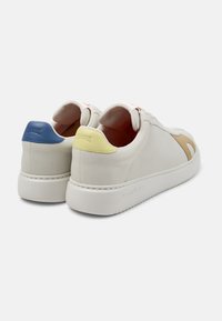 White leather sneakers featuring a beige side design, blue and yellow heel accents, and a textured white rubber sole.