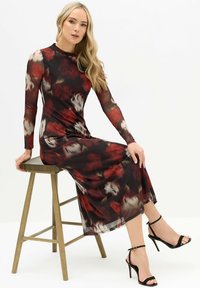 Vestido de manga larga con estampado floral en rojo y negro, hecho de un material ligero y transparente. Combinado con sandalias de tacón alto negras con tiras.