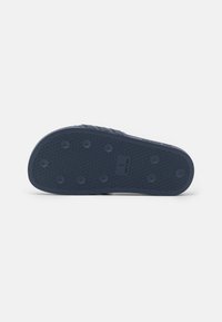 Blue rubber shoe sole featuring a textured pattern with circular grips and a logo. The design is flat with no raised heel.