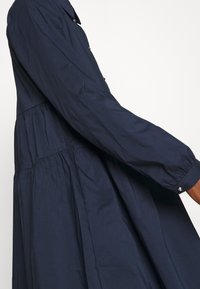 Mörkblå långärmad klänning i mjukt tyg, med en samlad nederdel, knäppte manschetter och en klassisk kragdesign.