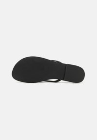Sandale negre plate cu o talpă din cauciuc neted, design minimalist și bretele subțiri. Talpa are o textură subtilă pentru aderență.