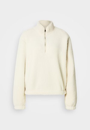 Felpa in pile color crema con collo alto, mezza cerniera, vestibilità ampia e polsini a costine. Texture morbida con fodera interna liscia.