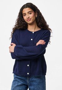 Navy knitted cardigan with long sleeves, round neckline, and five white buttons down the front. Casual fit and textured fabric.