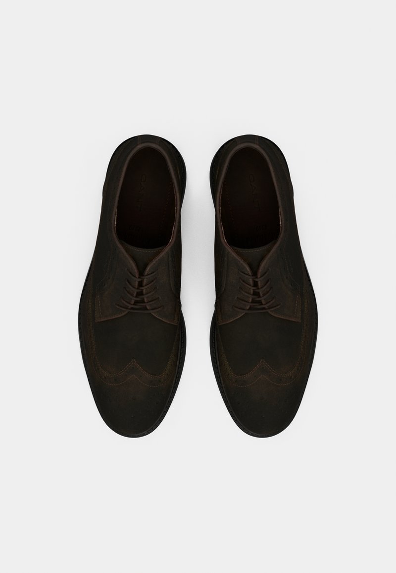 Chaussures en daim marron foncé avec un design à bout fleuri, bout rond et fermeture à lacets. Présentent des coutures détaillées et une tige lisse et texturée.