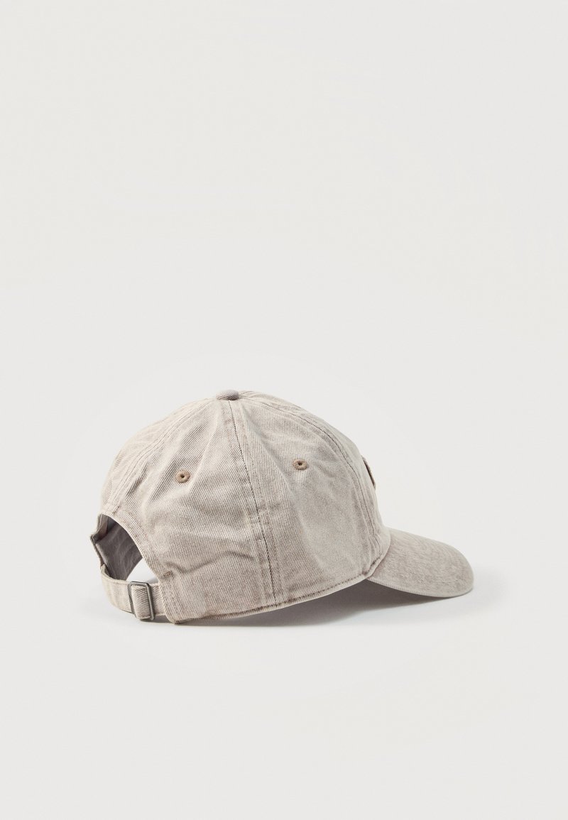Gorra de béisbol beige de algodón con correa ajustable, seis ojetes de ventilación y visera curvada, mostrada de lado sobre un fondo blanco.