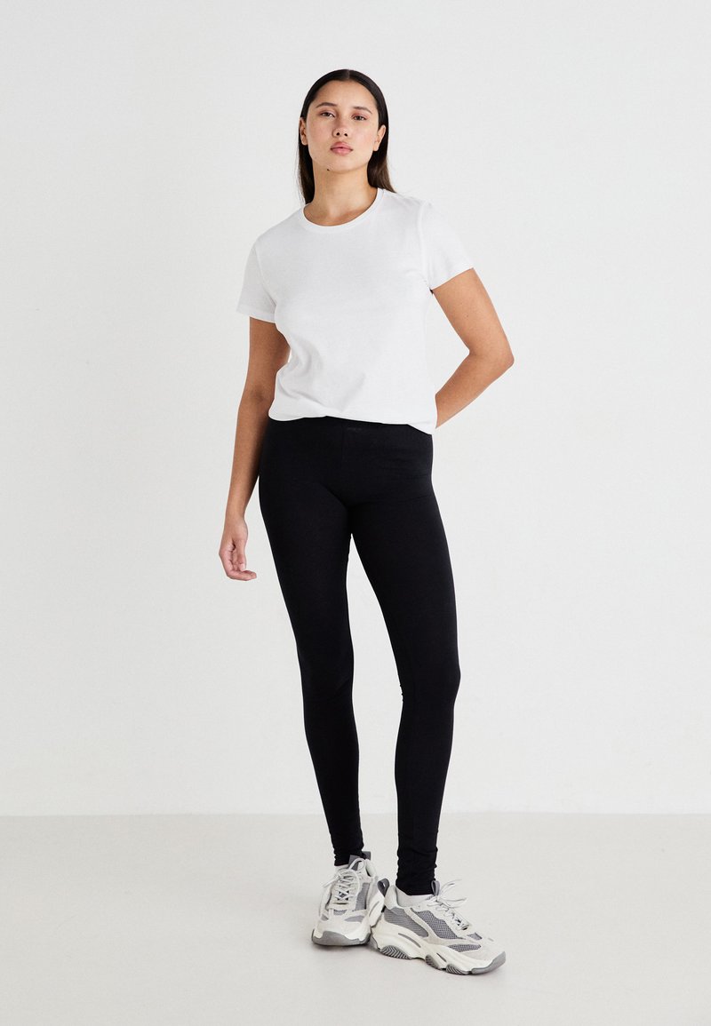 Svart leggings laget av elastisk stoff, parret med en tettsittende hvit t-skjorte. Antrekket er fullført med kraftige grå joggesko.