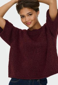 Maglione bordeaux a maglia con collo rotondo, maniche ampie e finitura testurizzata, abbinato a jeans di denim scuri.