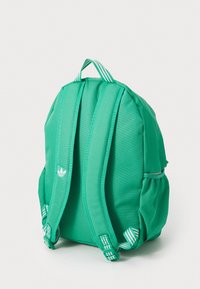 Πράσινο σακίδιο φτιαγμένο από ύφασμα με μαξιλαρωμένες ιμάντες και χειρολαβή στην κορυφή. Διαθέτει λευκές ρίγες και ένα μικρό λογότυπο στο πλάι.