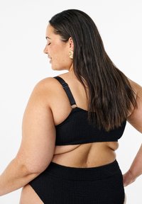 Zwarte textuur bikini top met verstelbare bandjes, gecombineerd met bijpassende hoog-taille onderkant, gezien vanaf de zijkant waardoor de ontwerpdetails worden benadrukt.