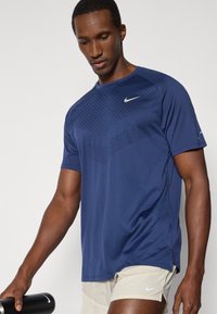 Σκούρο μπλε αθλητικό t-shirt της Nike με κοντά μανίκια, που διαθέτει υφή γεωμετρικού μοτίβου στο μπροστινό μέρος και σχέδιο με σκουρόχρωμο λαιμόκοψη.